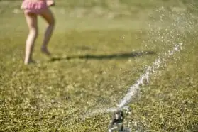 Girl in swim suit playing in the sprinkler on the lawn, water to keep your lawn healthy